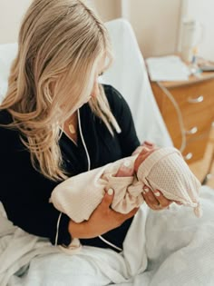 a woman holding a baby in her arms and listening to music on headphones while sitting in a hospital bed