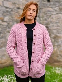 a woman standing in front of a stone wall wearing a pink cardigan