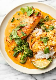 a white plate topped with fish and rice covered in sauce, garnished with cilantro