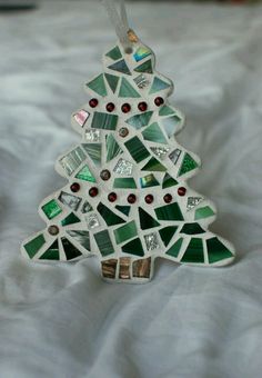 a glass christmas tree ornament sitting on top of a white bed sheet with red, green and silver decorations