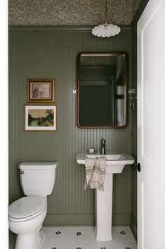 a white toilet sitting next to a sink in a bathroom under a framed painting on the wall