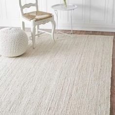 a white chair sitting on top of a wooden floor next to a rug and table