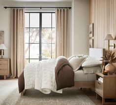 a bed sitting next to a window in a bedroom under a white and brown blanket