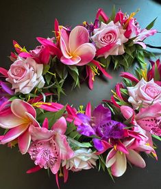 pink and purple flowers are arranged in a wreath on a black surface with green leaves