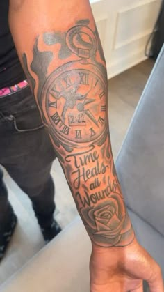 a person with a tattoo on their arm and wrist holding a clock in his hand