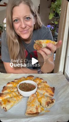 a woman holding up a piece of pizza with cheese and sauce in front of her