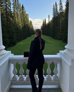 a woman standing on a balcony looking out at the grass and trees in the distance