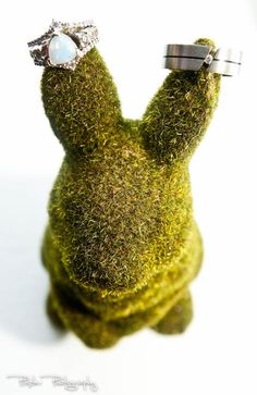 a ring that is sitting on top of a moss covered animal's head with a stone in the middle