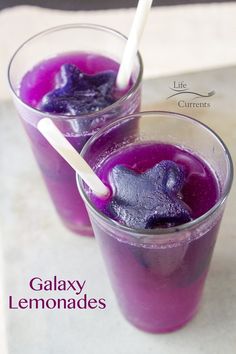 two glasses filled with purple liquid on top of a white tablecloth and the words galaxy lemonades above them