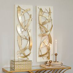 two metal art pieces sitting on top of a gold shelf next to a candle holder