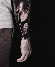 a man with a tattoo on his arm holding onto a flower and leaves in front of him