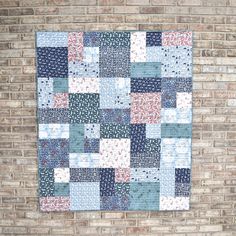 a blue and white patchwork quilt hanging on a brick wall