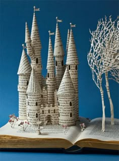 an open book with a castle made out of pages and trees on top of it