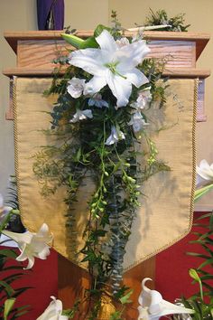 white flowers and greenery on display in front of a wall hanging from the ceiling