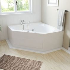 a white bath tub sitting under a window next to a rug on the floor in a bathroom