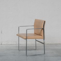 a tan leather chair sitting on top of a cement floor next to a white wall