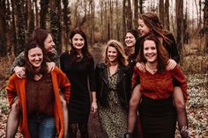 a group of women standing next to each other on a forest floor with trees in the background