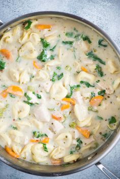 a pot filled with pasta and vegetables on top of a blue countertop next to silver spoons