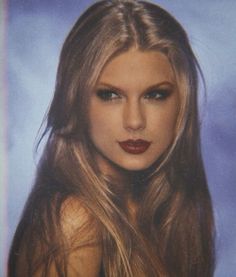 a woman with long blonde hair and red lipstick is posing for a photo in front of a blue background