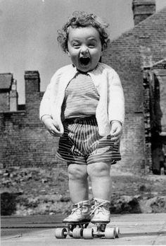 an old black and white photo of a toddler on a skateboard with his mouth open