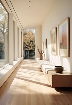 a long hallway with white walls and wooden flooring is lined with framed pictures on the wall