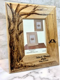 a wooden frame with two pictures in it on a marble countertop next to a tree