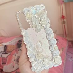 a person holding up a phone case with flowers and pearls on the back in front of a pink bed