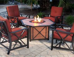 an outdoor fire pit with four chairs around it and a table on the ground next to it