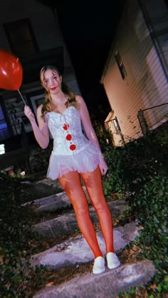 a woman in a white dress holding a red balloon and posing for the camera at night