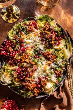 a large bowl filled with lots of food on top of a table next to wine glasses