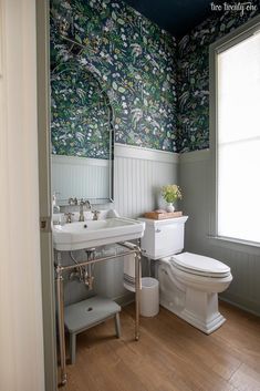 a white toilet sitting next to a sink in a bathroom under a window with blue and green wallpaper