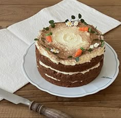 a cake with carrots and flowers on top sitting on a plate next to a knife