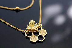 These images appear to show a beautifully crafted necklace set featuring a bee on a honeycomb pendant, with a delicate double-layer chain design. The pendant includes sparkling details on the honeycomb and a bee with gem accents. The upper layer is a simple, elegant chain with small gold beads, complementing the main pendant. Bee and Honeycomb Necklace Set This charming two-layer necklace set is inspired by nature's finest architects--the bees. The set features a delicate honeycomb pendant, ador Honeycomb Necklace, Layer Chain, Bee Honeycomb, Detailed Necklace, Layered Necklace Set, Layered Chains, Bee Charms, Chain Design, Layered Necklace