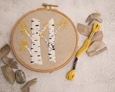 an embroidery project with yellow thread and white birch trees in the background, surrounded by leaves