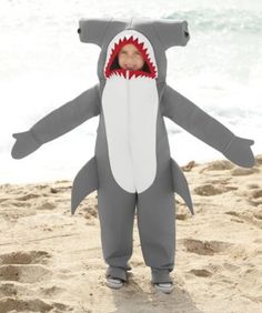 a baby in a shark costume standing on the beach