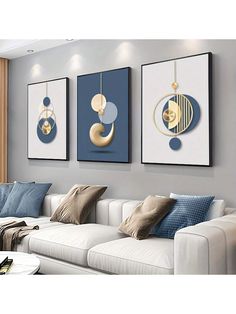 three paintings hang on the wall above a white couch in a living room with blue and gold accents