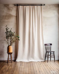 a room with a chair and a curtain in front of a window that has a potted plant next to it