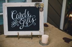 a sign that says cards and gifts on it next to a glass with a candle