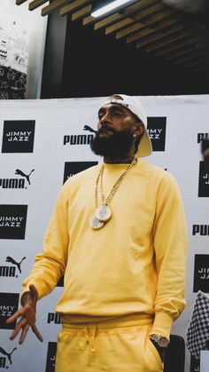 a man with a beard wearing a yellow sweatshirt and matching pants stands in front of a puma sign