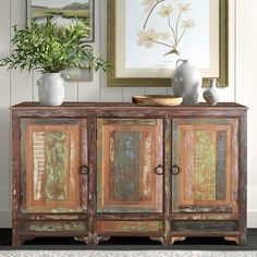 an old wooden sideboard with two vases on top and one potted plant in the corner