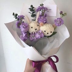 a person holding a bouquet of flowers with purple ribbons around it's ends and two stuffed animals in the middle