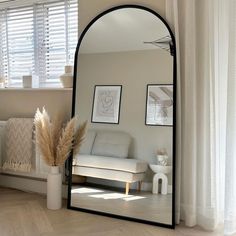 a mirror sitting on top of a wooden floor next to a white couch and window