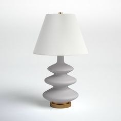 a table lamp with a white shade on it's side and a gold base