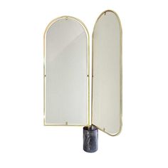 a large mirror sitting on top of a black vase next to a white wall mounted mirror