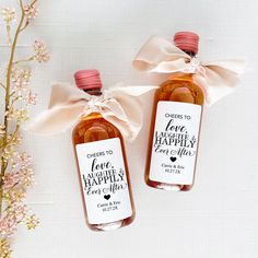 two personalized honey bottles tied with pink ribbon and bow on white surface next to flowers