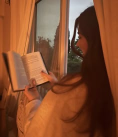 a woman reading a book while looking out the window