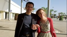 a man and woman standing next to each other in front of a building with palm trees