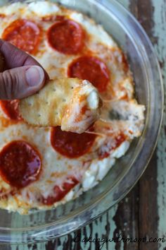 a hand holding a piece of pizza with cheese and pepperoni on it, over a glass plate