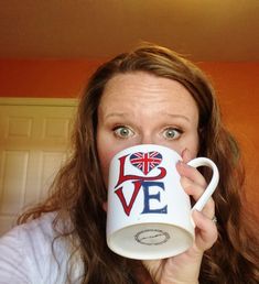 a woman holding up a coffee mug with the word love painted on it in front of her face