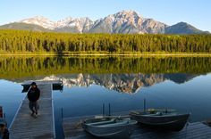 two boats are docked at the end of a wooden dock with mountains in the background